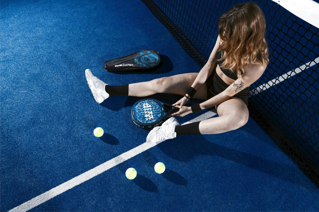 a woman sitting on a padel court holding a padel racquet